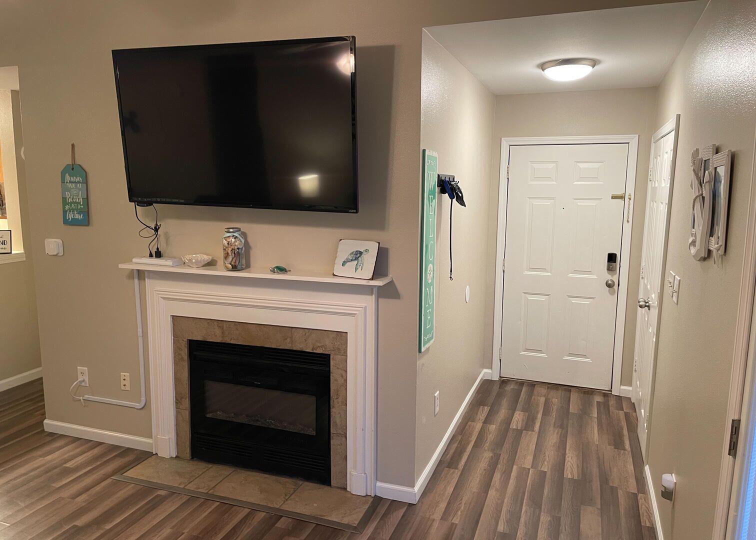 A hallway with a fireplace, a mounted TV, and a door with a 'WELCOME' sign.
