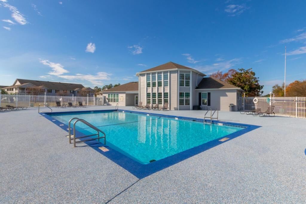 Una piscina con agua cristalina azul, rodeada por una valla blanca, y un edificio con grandes ventanales al fondo.
