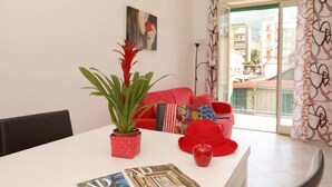 A modern living room with a white table, red sofa, and a balcony with patterned curtains. - Suite Pina Ocean in Sorrento (Sorrento)
