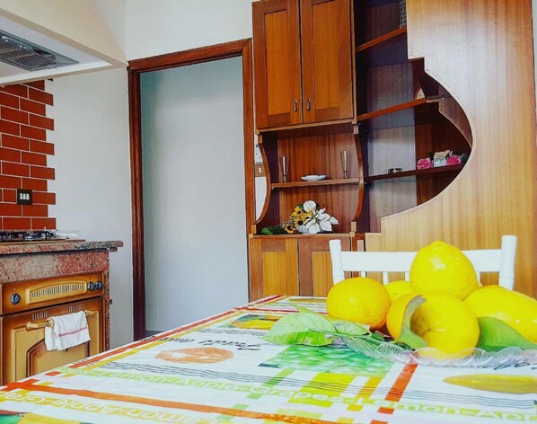A kitchen with a brick wall, wooden cabinets, and a stove. There is a table with lemons and a tablecloth. - Suite Pina Ocean in Sorrento (Sorrento)