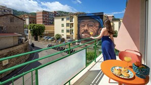 A balcony with a view of a street, a table with food and drinks, and a mural on the wall. - Suite Pina Ocean in Sorrento (Sorrento)