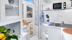 A modern kitchen with white cabinetry, a built-in microwave, and a large window offering a scenic view. - Relaxing Positano in Positano (Positano)