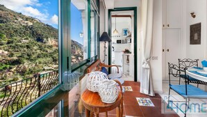 A balcony with a view of a mountainous landscape, a dining area with a table and chairs, and a kitchen visible through an open door. - Relaxing Positano in Positano (Positano)