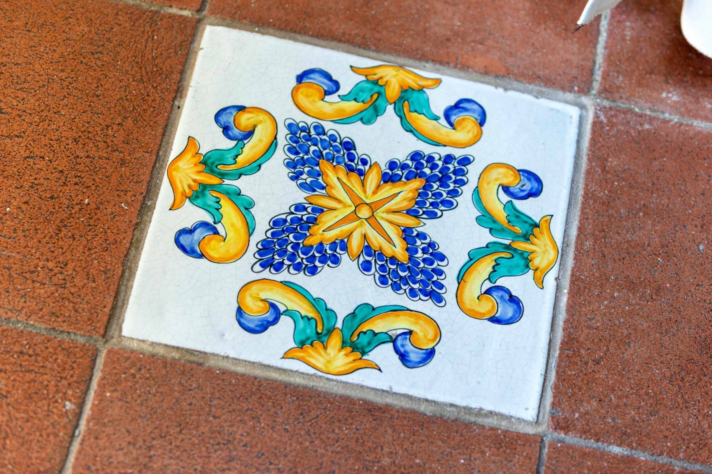 Un carreau de céramique de forme carrée, orné d’un motif floral bleu et jaune.