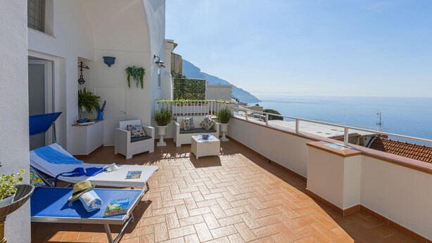 Ein sonnendurchfluteter Balkon mit Terrasse, weißen Wänden und Meerblick.