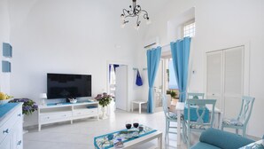 Ein helles Wohnzimmer mit Fernseher, weißen Möbeln und Meerblick.