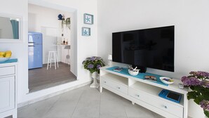 Ein modernes Wohnzimmer mit Flachbildfernseher, einer weißen Unterhaltungsanlage und einer Küche im Hintergrund.