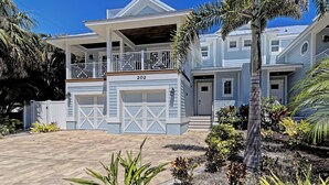 A two-story house with a covered porch, a garage, and a well-maintained garden with various plants. - Oasis by the Beach managed by the Beach Retreats (Holmes Beach)