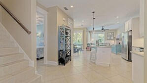 A spacious kitchen with a central island, a dining area with a table and chairs, and a staircase leading to another level. - Oasis by the Beach managed by the Beach Retreats (Holmes Beach)