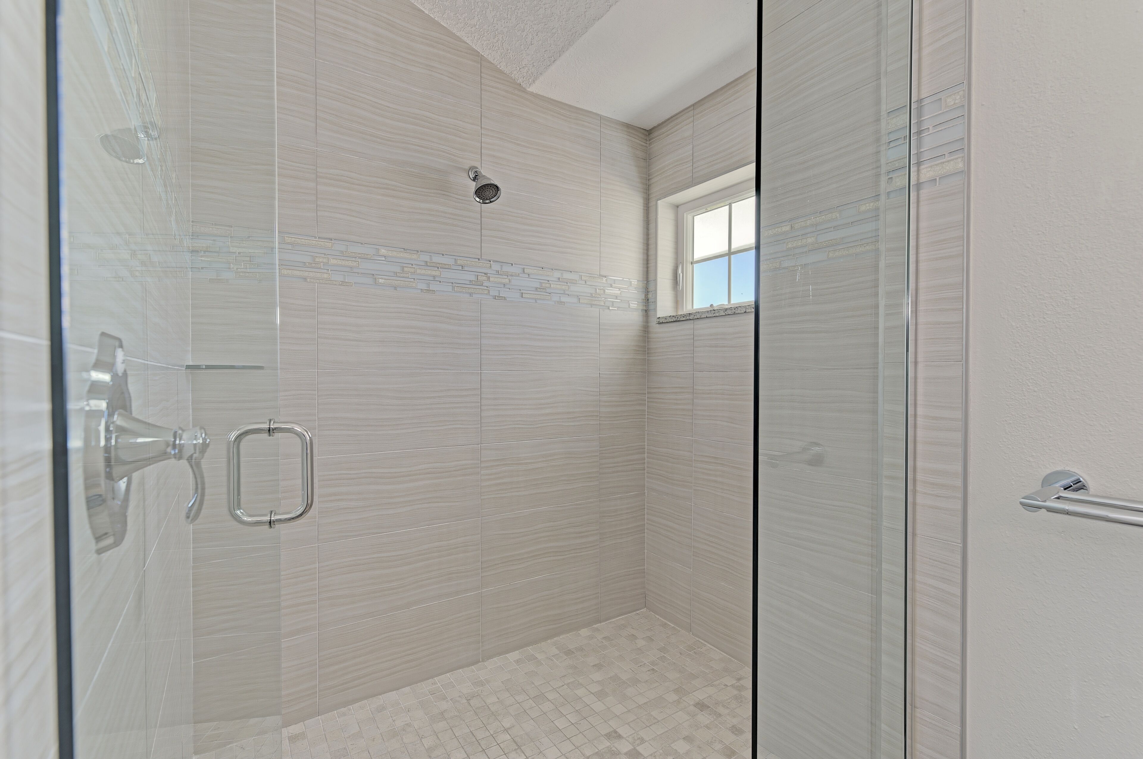 A glass-enclosed shower with a tiled floor and a small window.