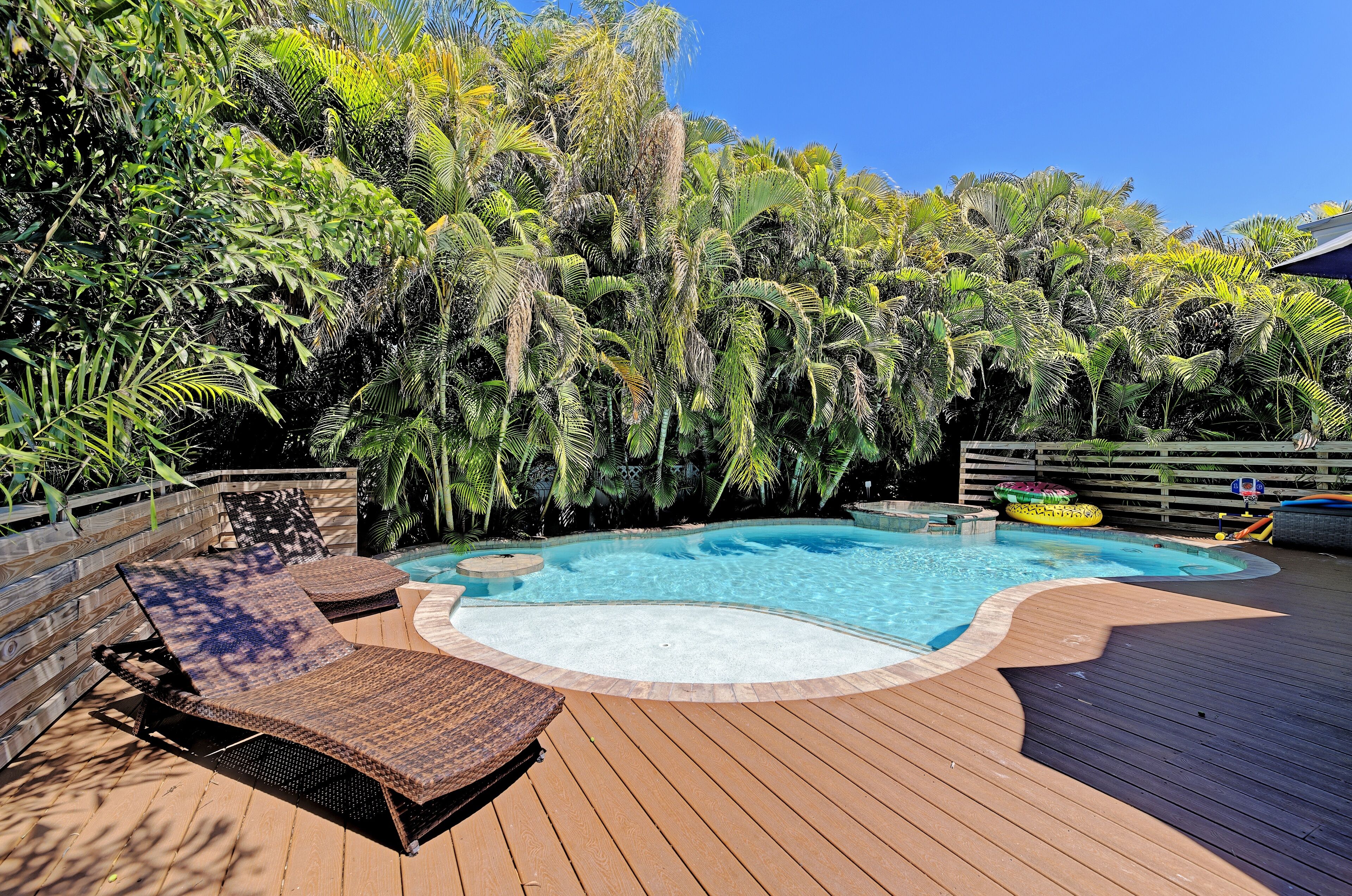 A swimming pool with a wooden deck, surrounded by lush tropical foliage.