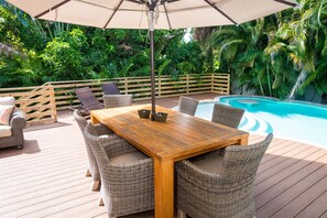A wooden deck with wicker furniture, a pool, and lush greenery. - Oasis by the Beach managed by the Beach Retreats (Holmes Beach)