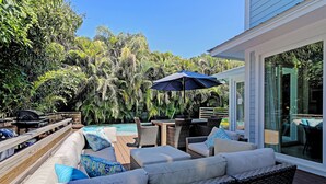 An outdoor patio with wicker furniture, a pool, and lush greenery. - Oasis by the Beach managed by the Beach Retreats (Holmes Beach)