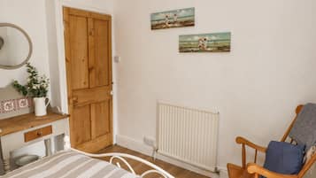 A bedroom with a wooden door, a bed with a striped bedspread, a wooden chair with a blue cushion, and two paintings on the wall.
