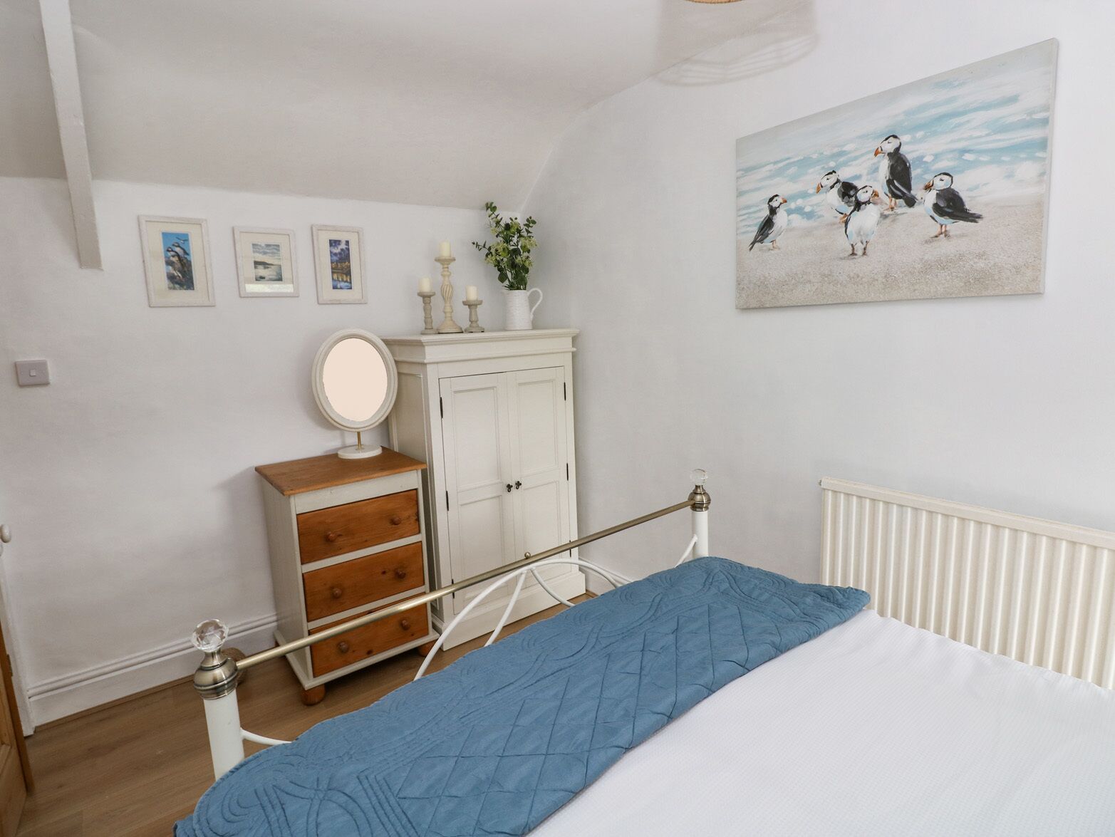 A bedroom with a bed, a dresser, a mirror, a radiator, and a wall with framed pictures.
