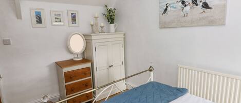 A bedroom with a bed, a dresser, a mirror, a radiator, and a wall with framed pictures.