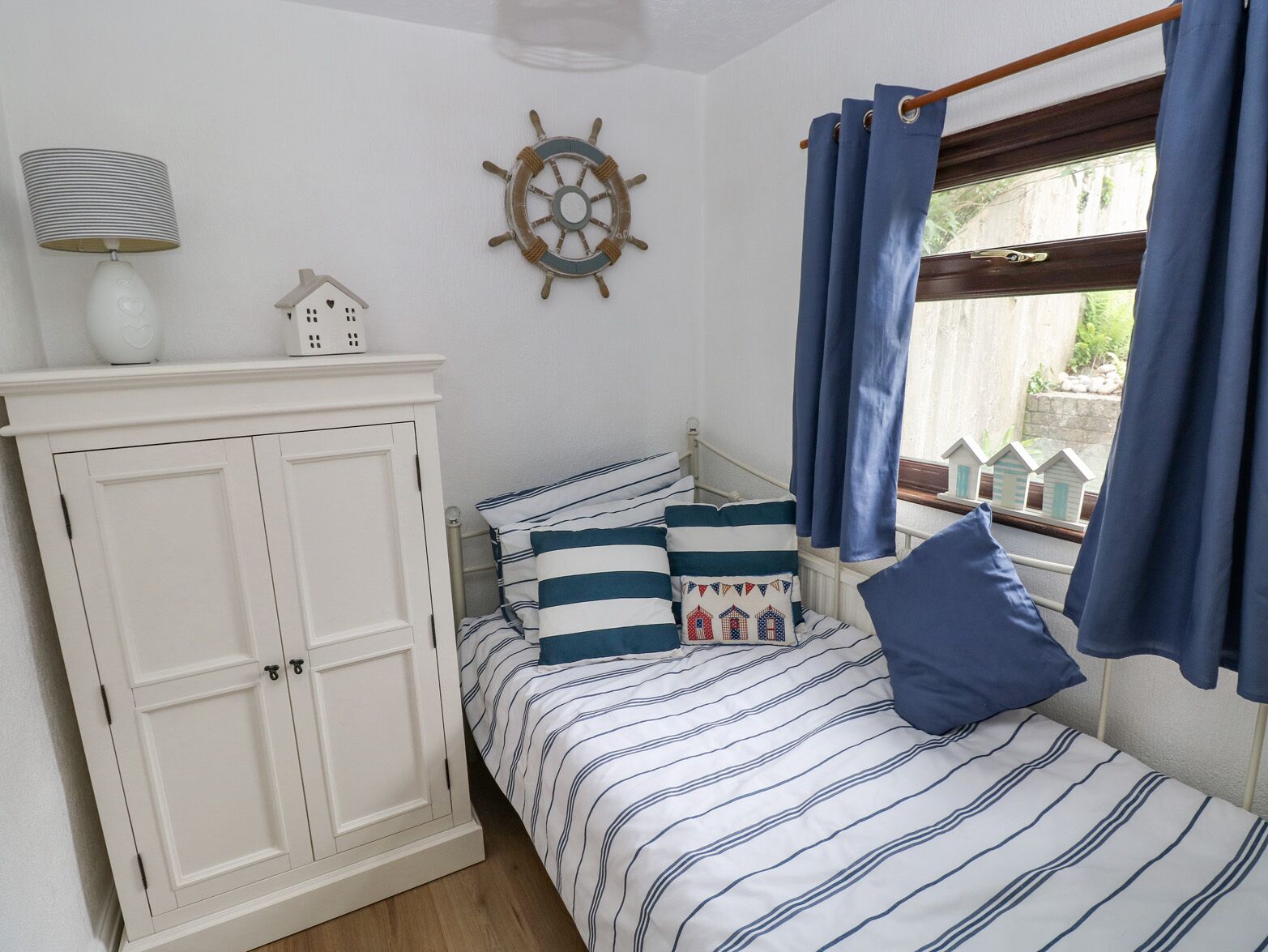 Une chambre à coucher avec un lit, une armoire, un décor représentant un gouvernail de bateau et une fenêtre avec des rideaux.