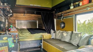 Een compact en overzichtelijk interieur van een camper, met een bed, zithoek en diverse voorzieningen zoals een kaart, een ventilator en opbergplanken.