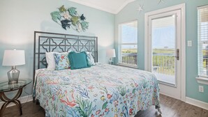 A bedroom with a bed, two bedside tables, a ceiling fan, and a view through the window. - Adventure Awaits by Ryson Vacation Rentals (Galveston)