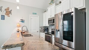 A modern kitchen with white cabinets, stainless steel appliances, and a granite countertop. - Adventure Awaits by Ryson Vacation Rentals (Galveston)