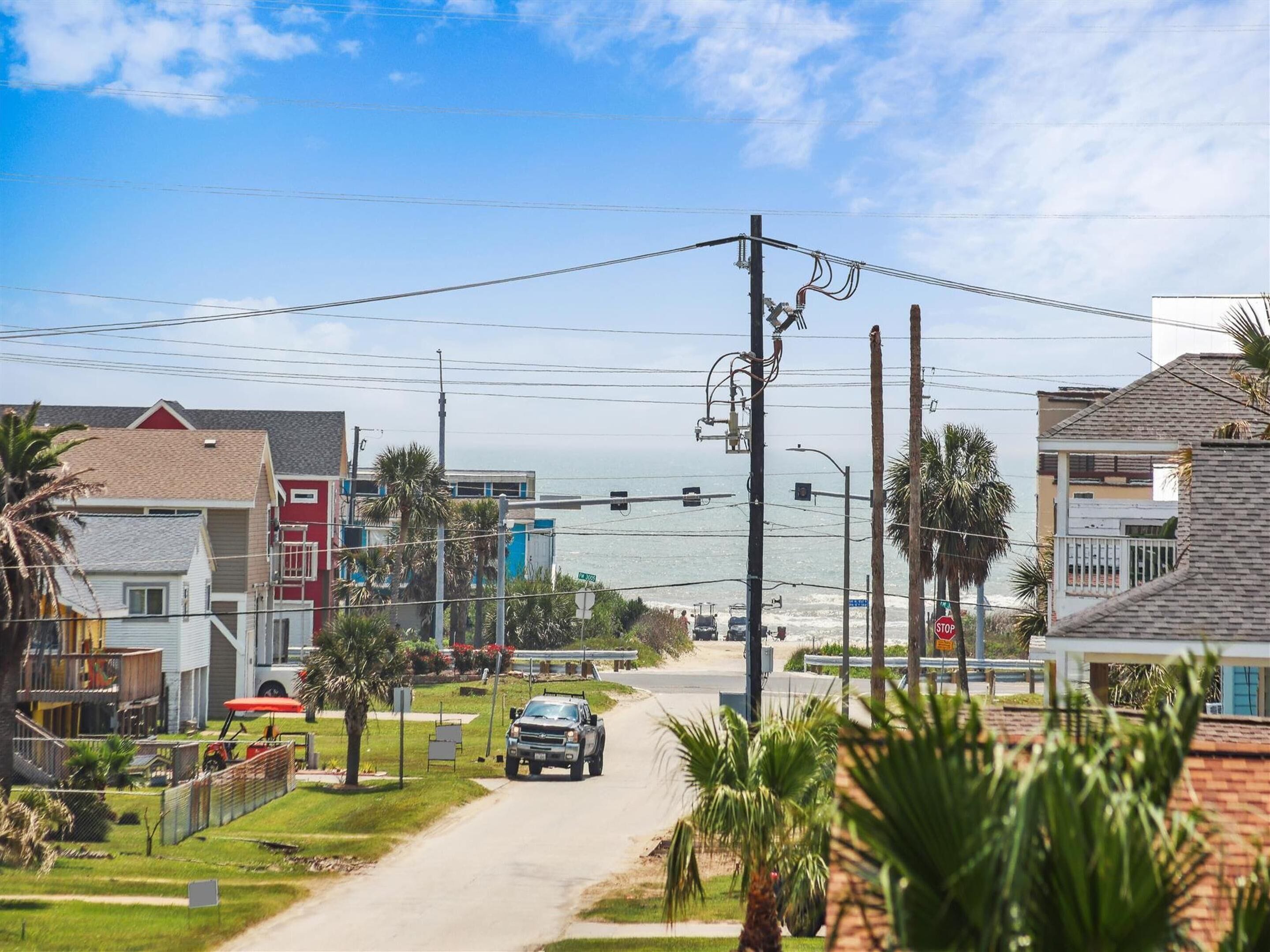 A coastal road with houses, palm trees, and a view of the ocean.