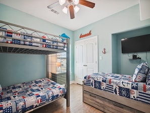 A room with bunk beds, a television, and a door with a 'beach' sign. - Adventure Awaits by Ryson Vacation Rentals (Galveston)