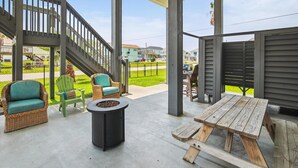En udendørs patio med fletmøbler, et bålsted og et træbord.