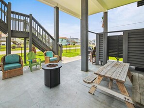 An outdoor patio with wicker furniture, a fire pit, and a wooden table. - Adventure Awaits by Ryson Vacation Rentals (Galveston)