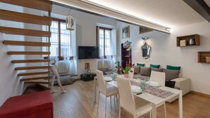 A modern living room with a dining area, wooden slats on the wall, a flat-screen TV, a sofa with green cushions, and a red bench. - Monalda Loft 2 (Florence)