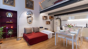 A modern living room with a red sofa, a dining table with white chairs, a kitchen area, and a ceiling with a string of lights. - Monalda Loft 2 (Florence)