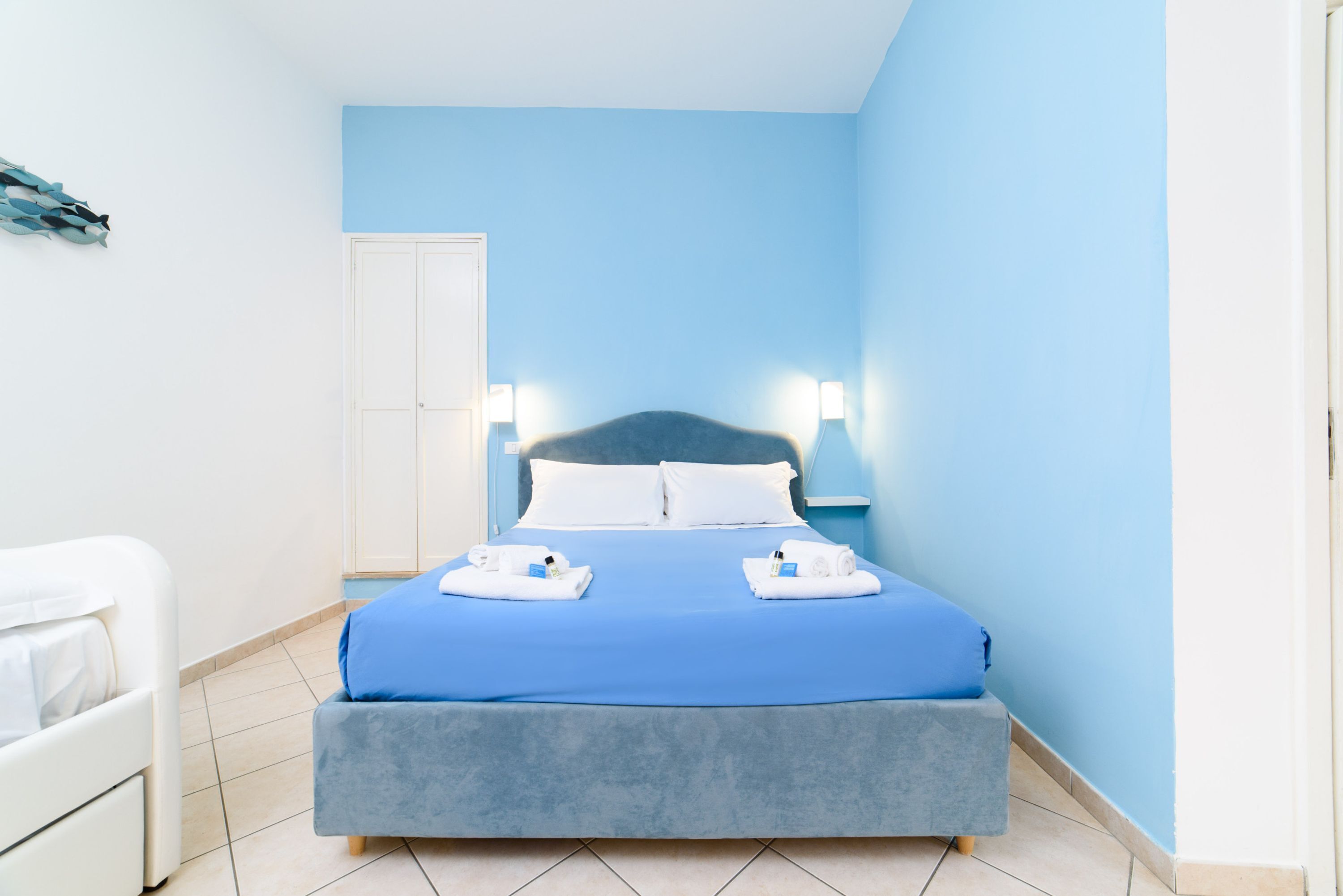 Una camera d'hotel con un letto, un armadio bianco e una parete blu.