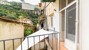 A balcony with a metal railing, a white door with a screen, and a view of a hillside with buildings and greenery. - Casa Annal in Sorrento (Sorrento)
