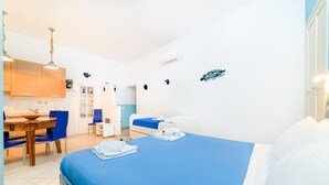 A modern hotel room with a large bed, a dining area with a wooden table and blue chairs, and a kitchenette. - Casa Annal in Sorrento (Sorrento)