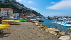 A coastal town with colorful kayaks lined up on the beach, a rocky shoreline, and buildings on a hillside in the background. - Casa Annal in Sorrento (Sorrento)