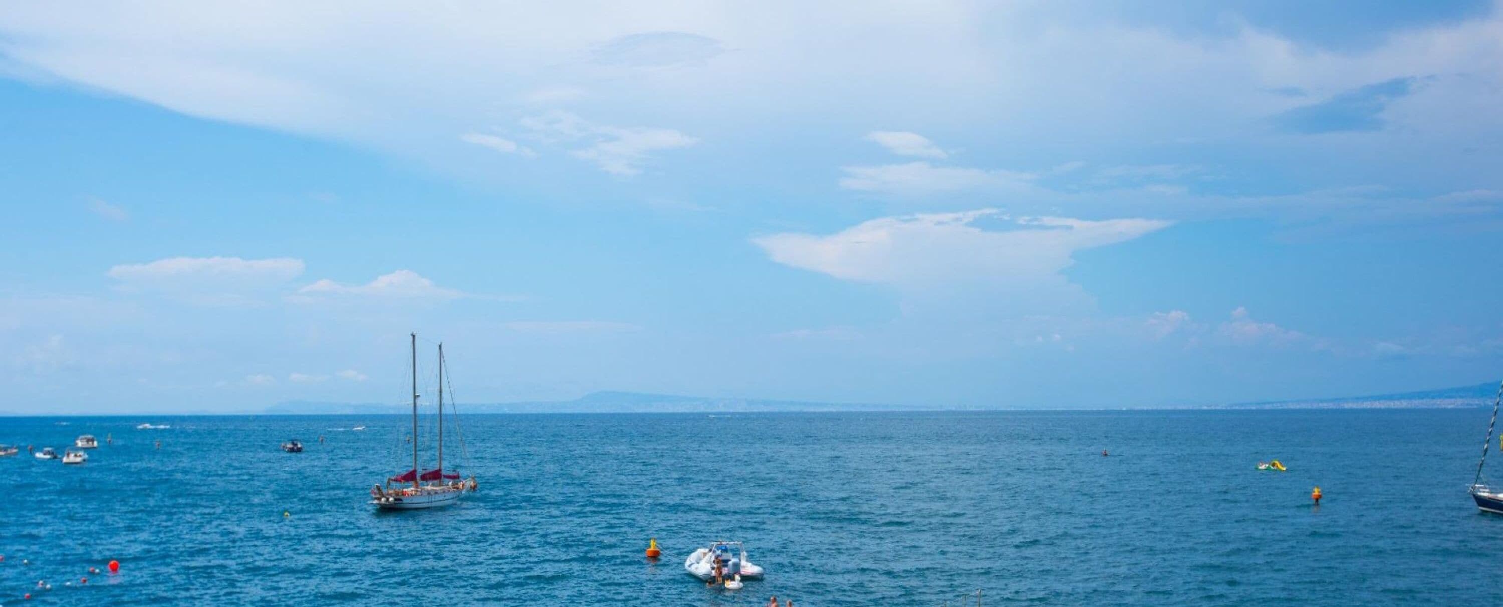 Une scène côtière avec un voilier et plusieurs petits bateaux sur l’eau.