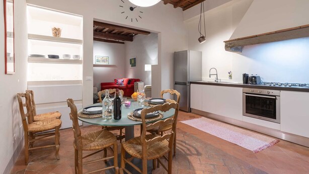 Une cuisine moderne avec un coin repas, comprenant une table ronde, des chaises en bois, un four encastré et une grande fenêtre donnant sur le jardin.