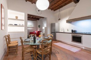 Een moderne keuken met eethoek, met een ronde tafel, houten stoelen, een inbouwoven en een groot raam met uitzicht op de tuin.