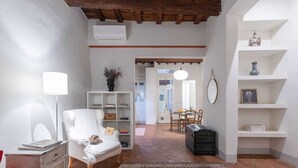 Un salon chaleureux avec un fauteuil blanc, une bibliothèque, un tapis à motifs et une commode en bois.