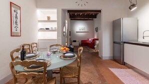 Un coin repas avec une table ronde dressée pour quatre personnes, des chaises en bois, une table en verre et une horloge au mur.