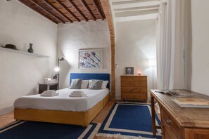 Een slaapkamer met een bed, nachtkastje, kaptafel en een schilderij aan de muur.