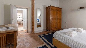Une chambre à coucher avec un lit en bois, un bureau avec des papiers, une armoire et une vue sur une autre pièce.