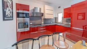 A modern kitchen with red cabinetry, stainless steel appliances, and a glass dining table. - Amazing Views of Spinola Bay in Heart of St.julians (St. Julian's)