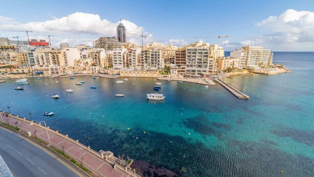 A coastal cityscape with a marina filled with boats, a prominent tower, and a mix of residential and commercial buildings. - Amazing Views of Spinola Bay in Heart of St.julians (St. Julian's)