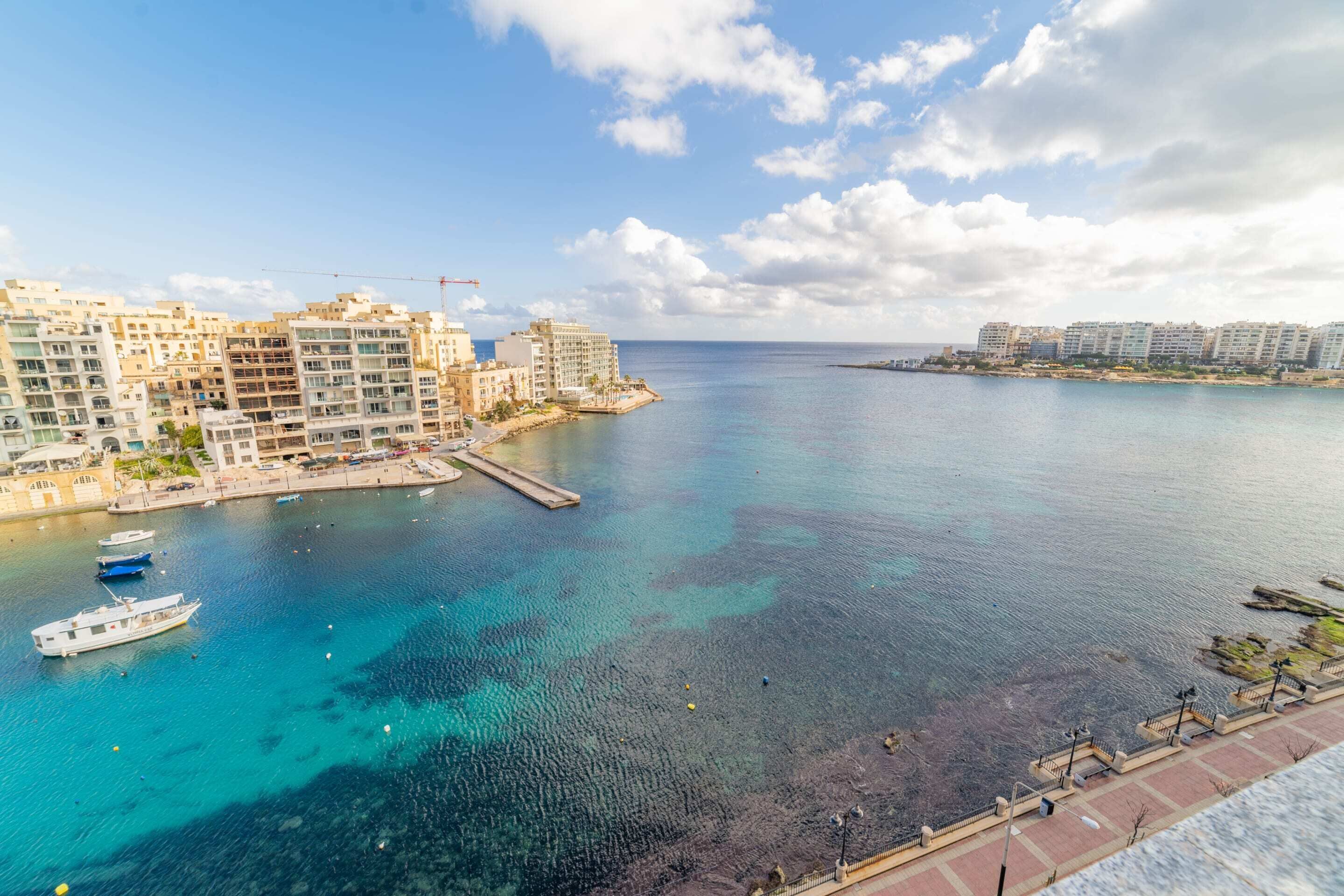 Un paisaje urbano costero con rascacielos, un puerto deportivo con barcos y un mar azul y despejado.