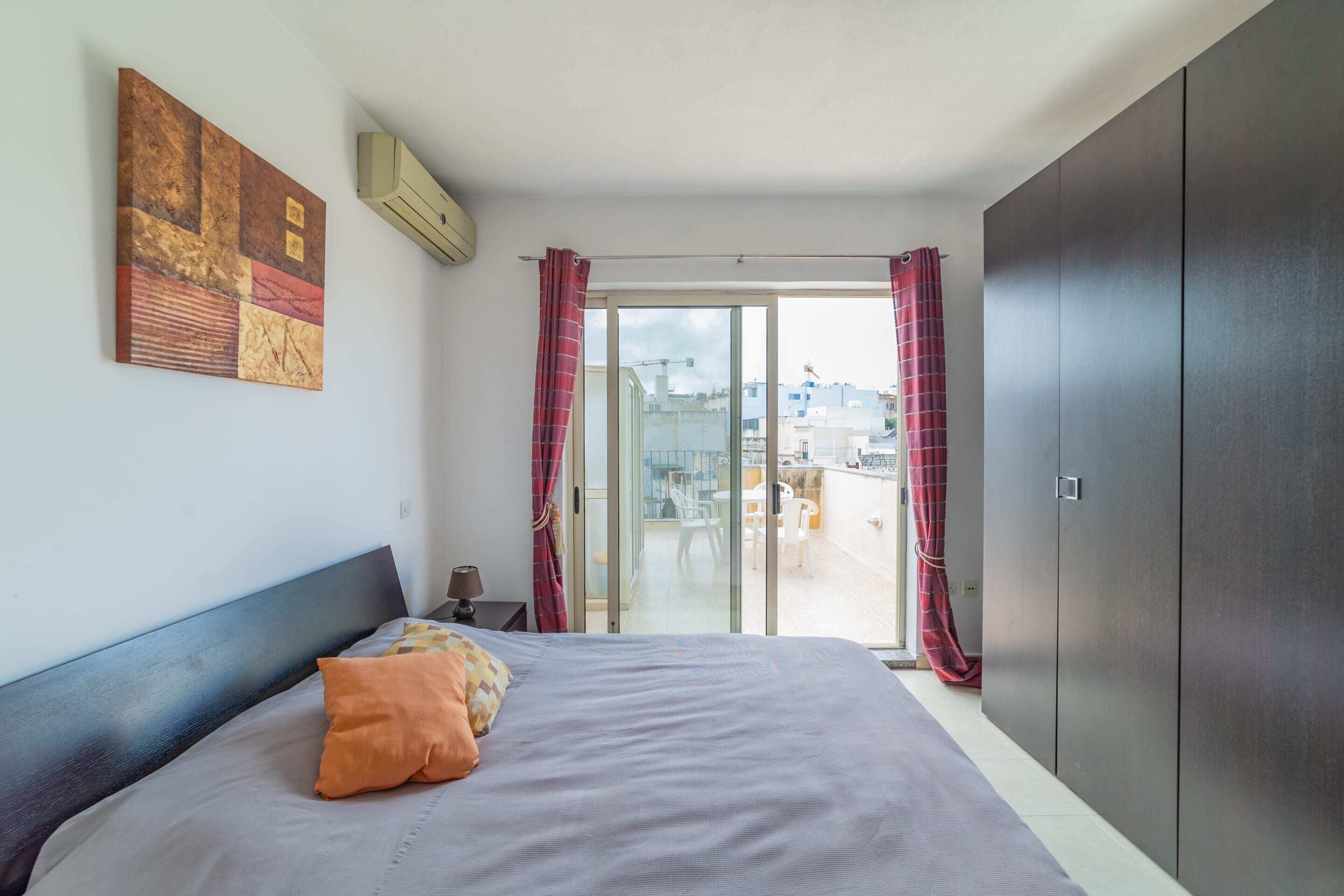 Et soveværelse med seng, garderobeskab, skydedør til en balkon og en loftsvifte.