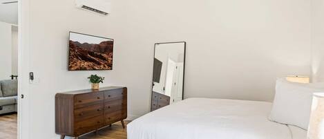 Un dormitorio con cama, cómoda, espejo y aire acondicionado instalado en la pared.