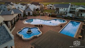 Un quartier résidentiel doté d’une piscine entourée de maisons, d’un espace patio et offrant une vue sur les montagnes en arrière-plan.