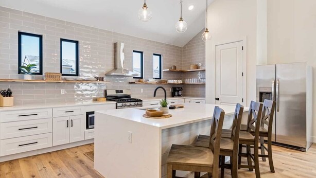 Une cuisine moderne avec des meubles blancs, un îlot central et un réfrigérateur en acier inoxydable.
