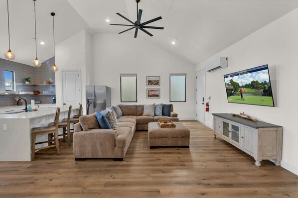 A modern living room with a sectional sofa, ottoman, and a TV mounted on the wall. - Desert Bungalow #h8 3 Bedroom Home (Hurricane)