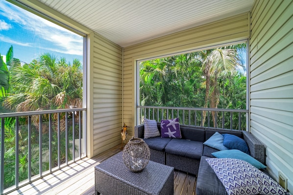 A covered balcony with a wicker sofa, cushions, and a woven basket.